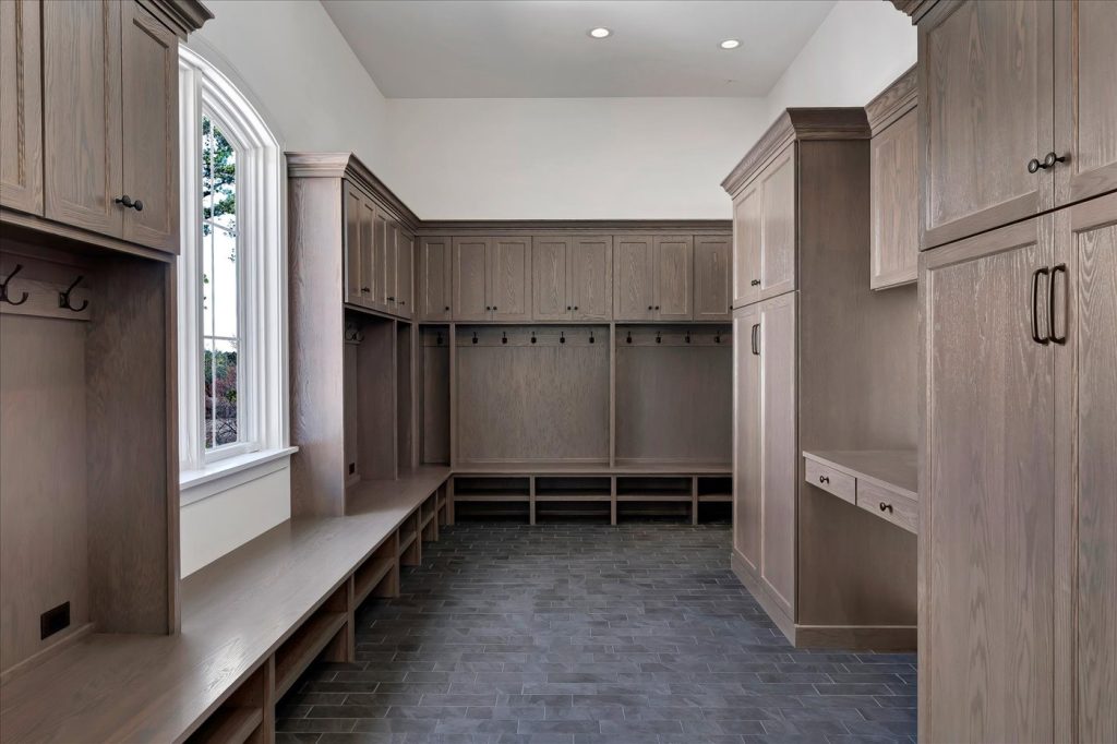 Stockell Custom Homes photo of luxury mudroom with dark gray tile floor and stained cabinetry & shelving